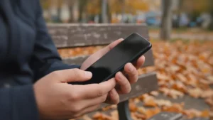 Persona sujetando su teléfono con ambas manos mientras revisa un chat sentada en un banco del parque